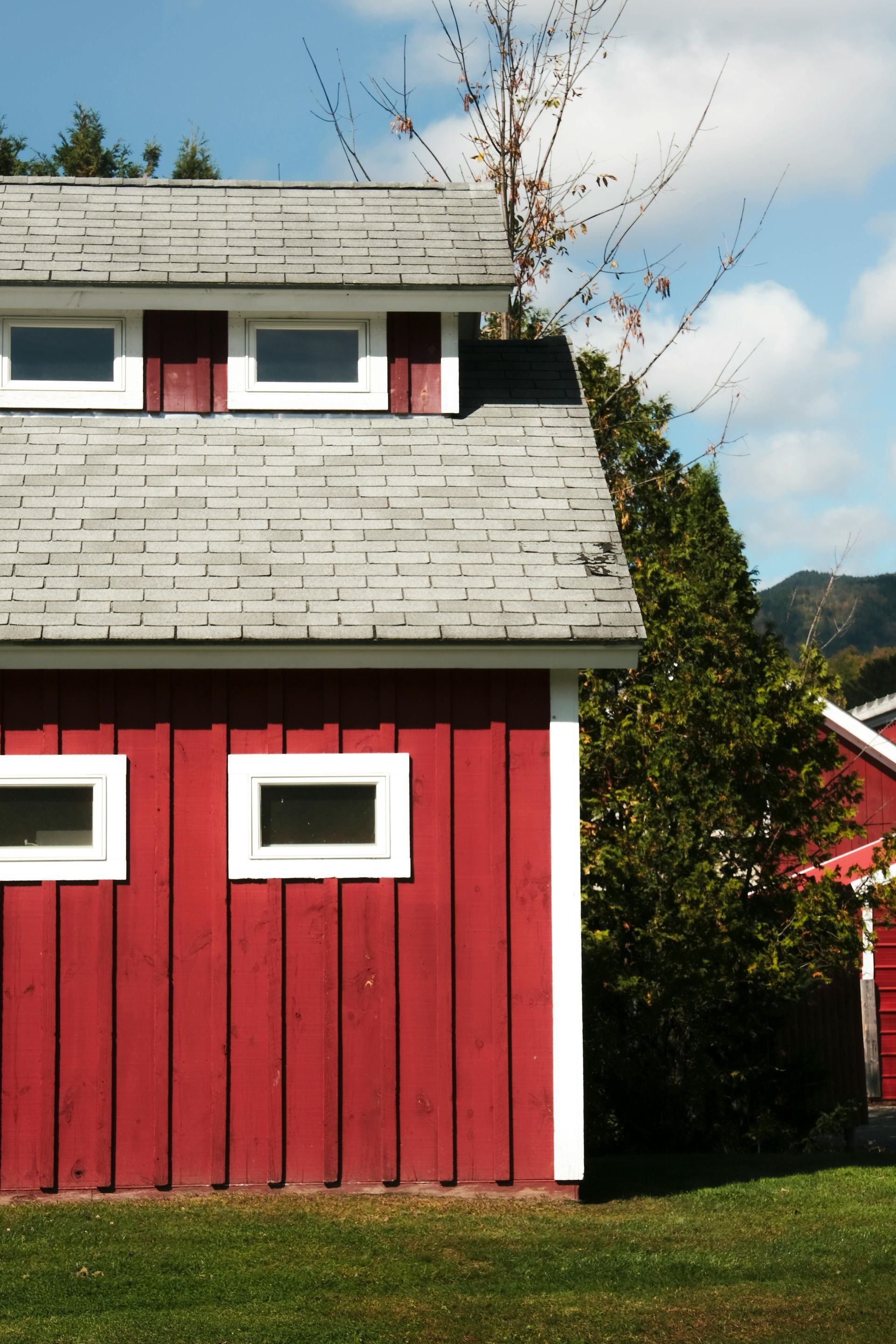 Red wooden house with white-trimmed windows and a gray roof under a blue sky.
