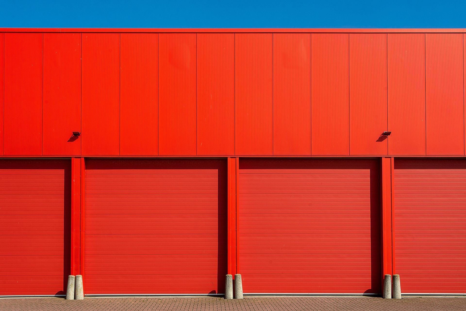 Red industrial building with four closed roll-up doors under a bright red facade.
