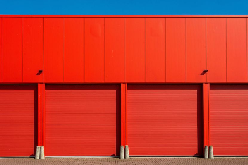Red industrial building with four closed roll-up doors under a bright red facade.