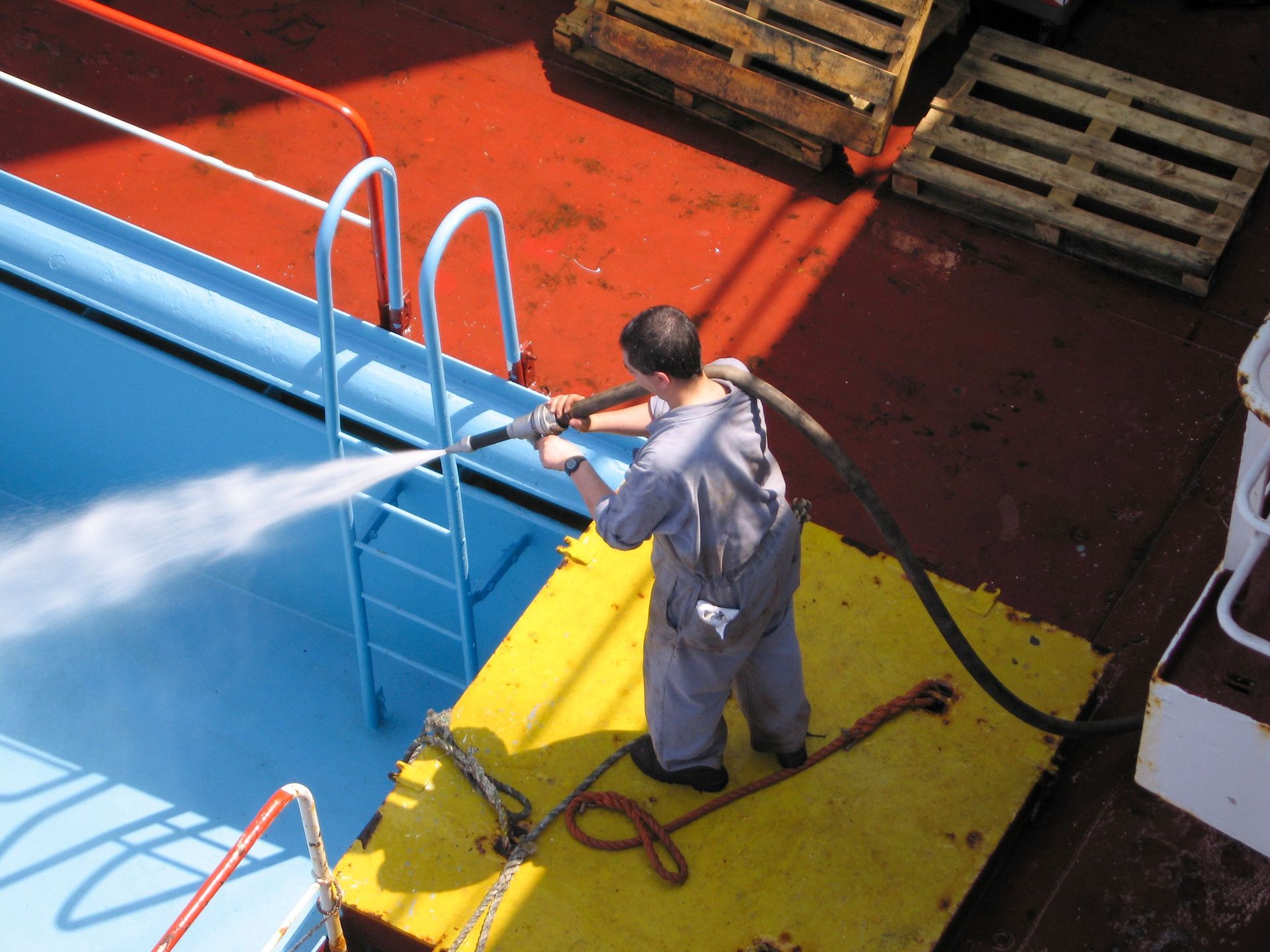 Worker power-washing a blue ship deck beside a yellow platform