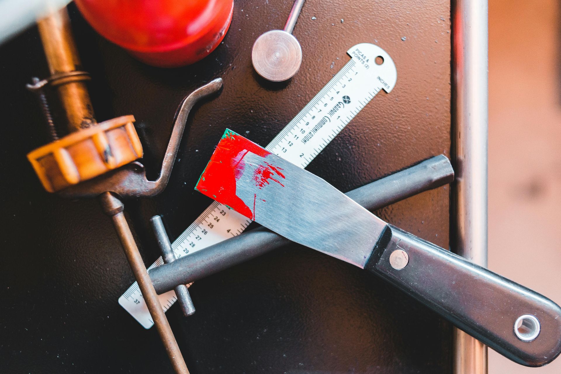 Hand saw and wrench coated with red paint on a workbench, with a magnifying glass nearby