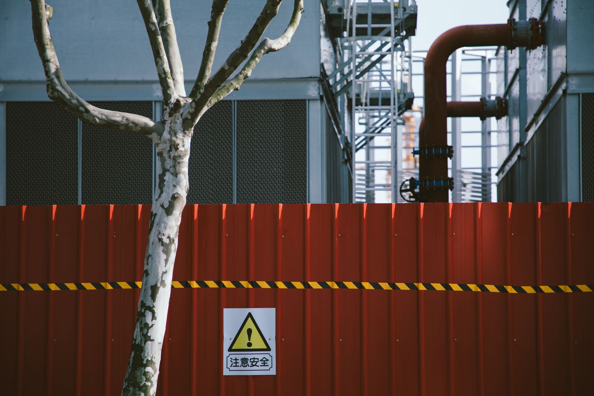 Industrial facility behind a red fence with warning sign and exposed pipes