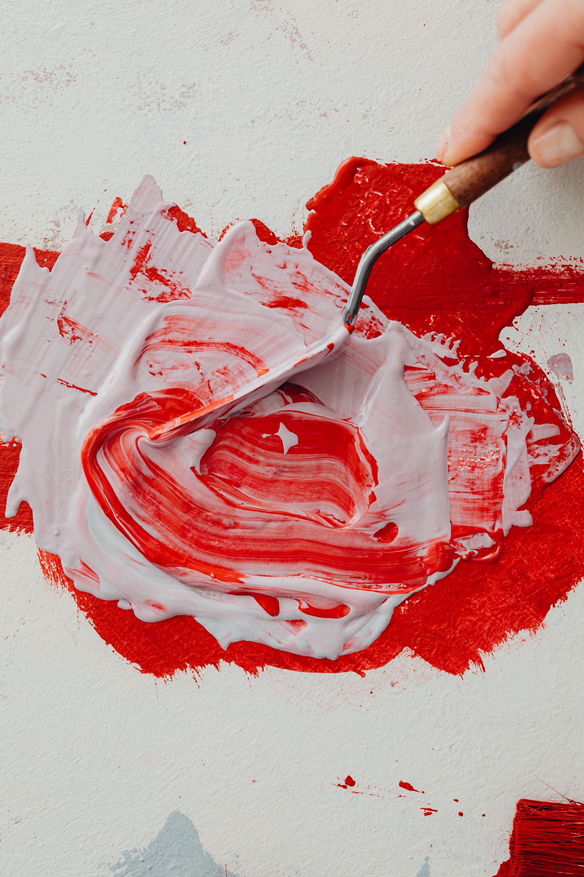 Hand holding a palette knife mixing red and white paint on a canvas
