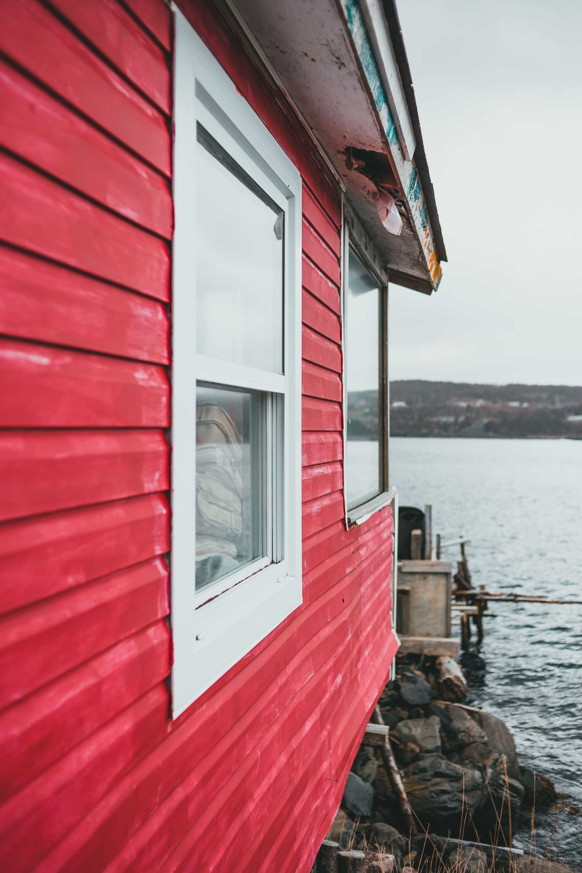 Red wooden house beside calm water on a cloudy day
