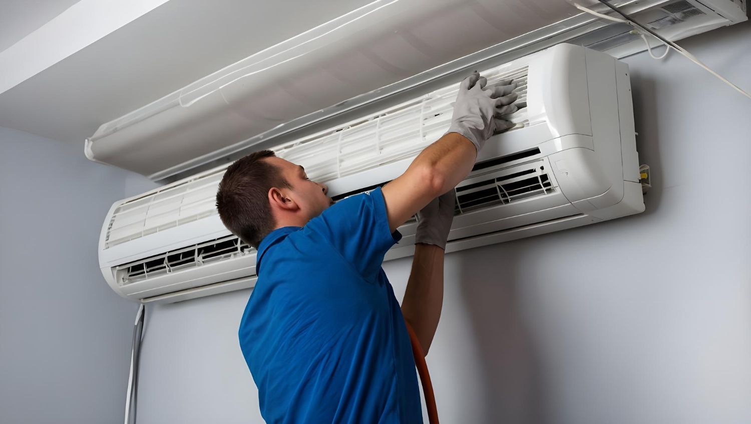 Man in blue shirt servicing a white wall-mounted air conditioner.