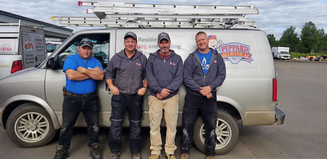 Four people posing beside a silver service van with ladders on top in a parking lot.
