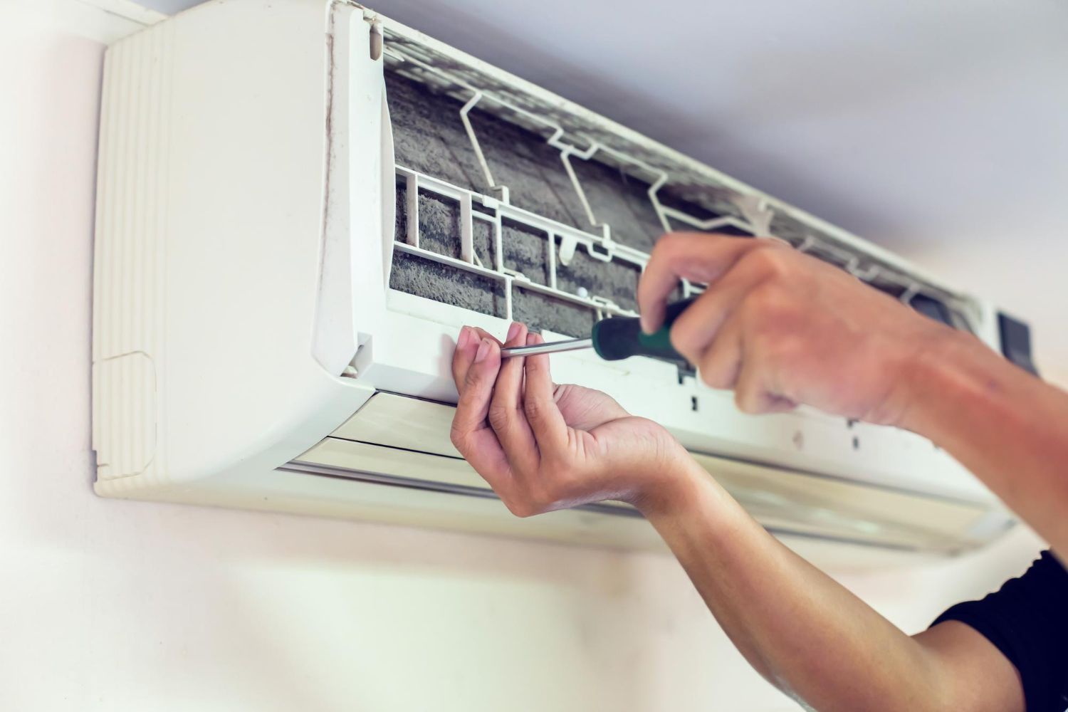 A person using a screwdriver to open the casing of a wall-mounted air conditioner unit for maintenance.