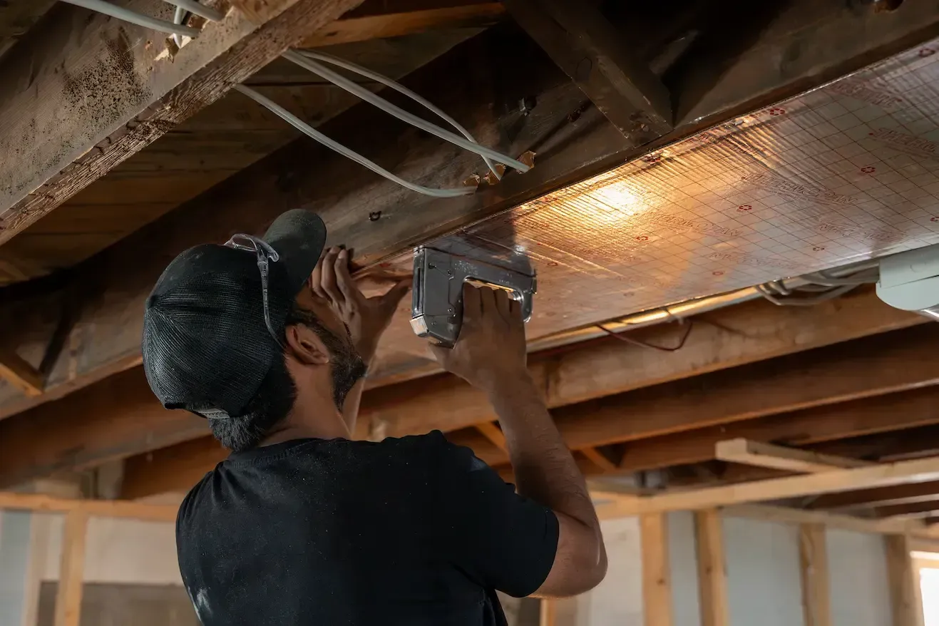 Worker drilling into a wooden ceiling beam in a house under construction