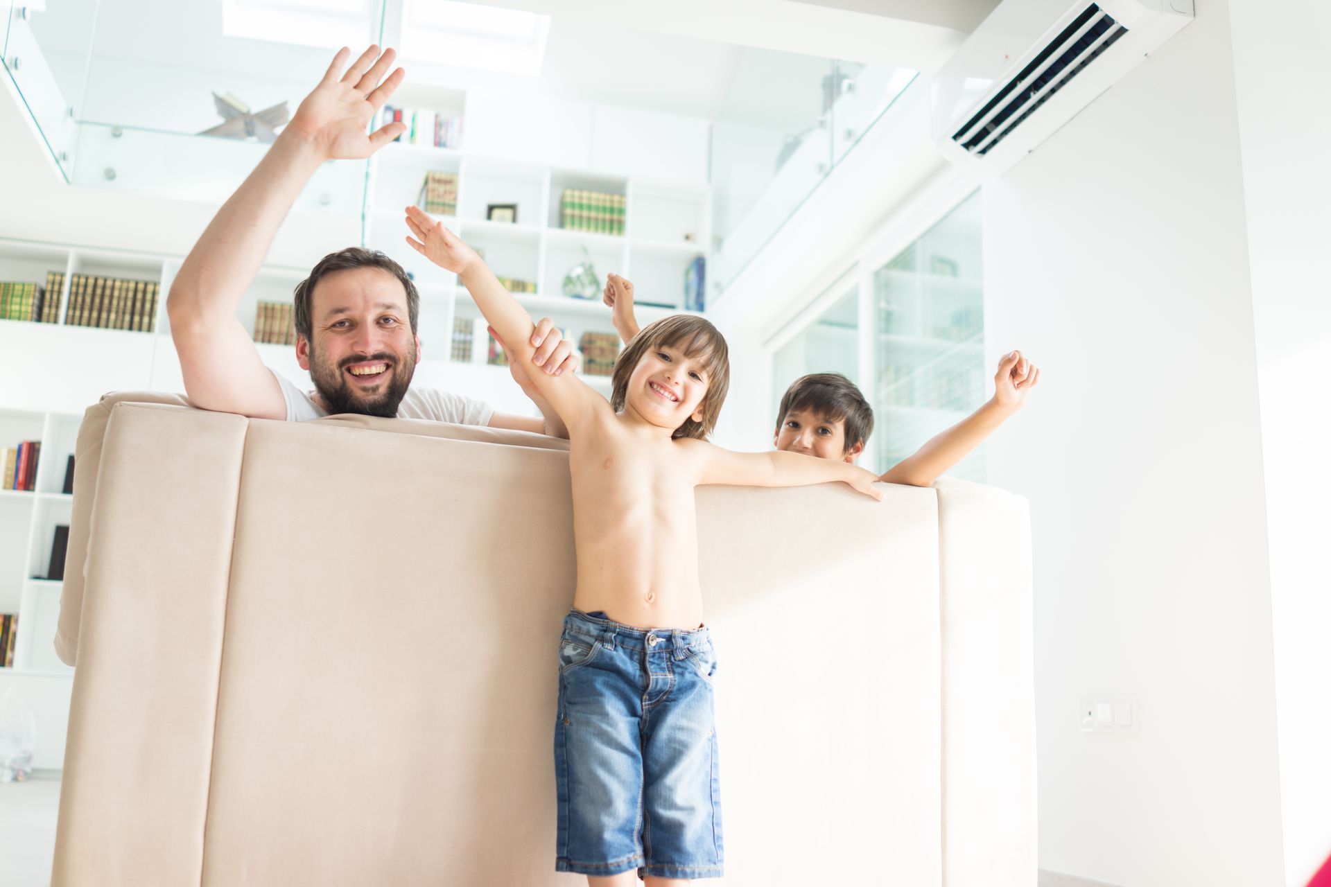 Family waving from behind a cardboard moving box in a bright home interior