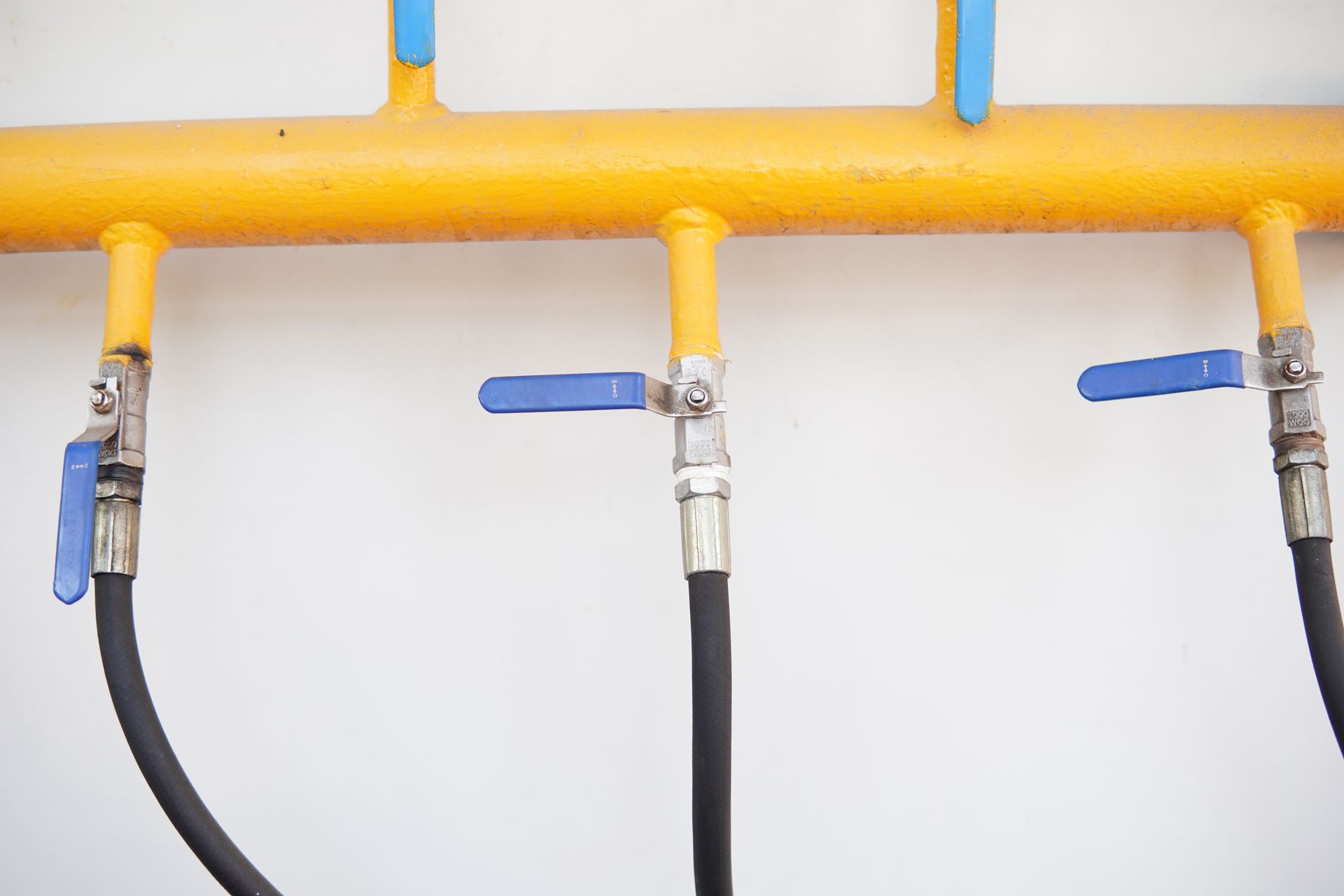 Yellow gas pipe with three blue-handled valves and black hoses attached