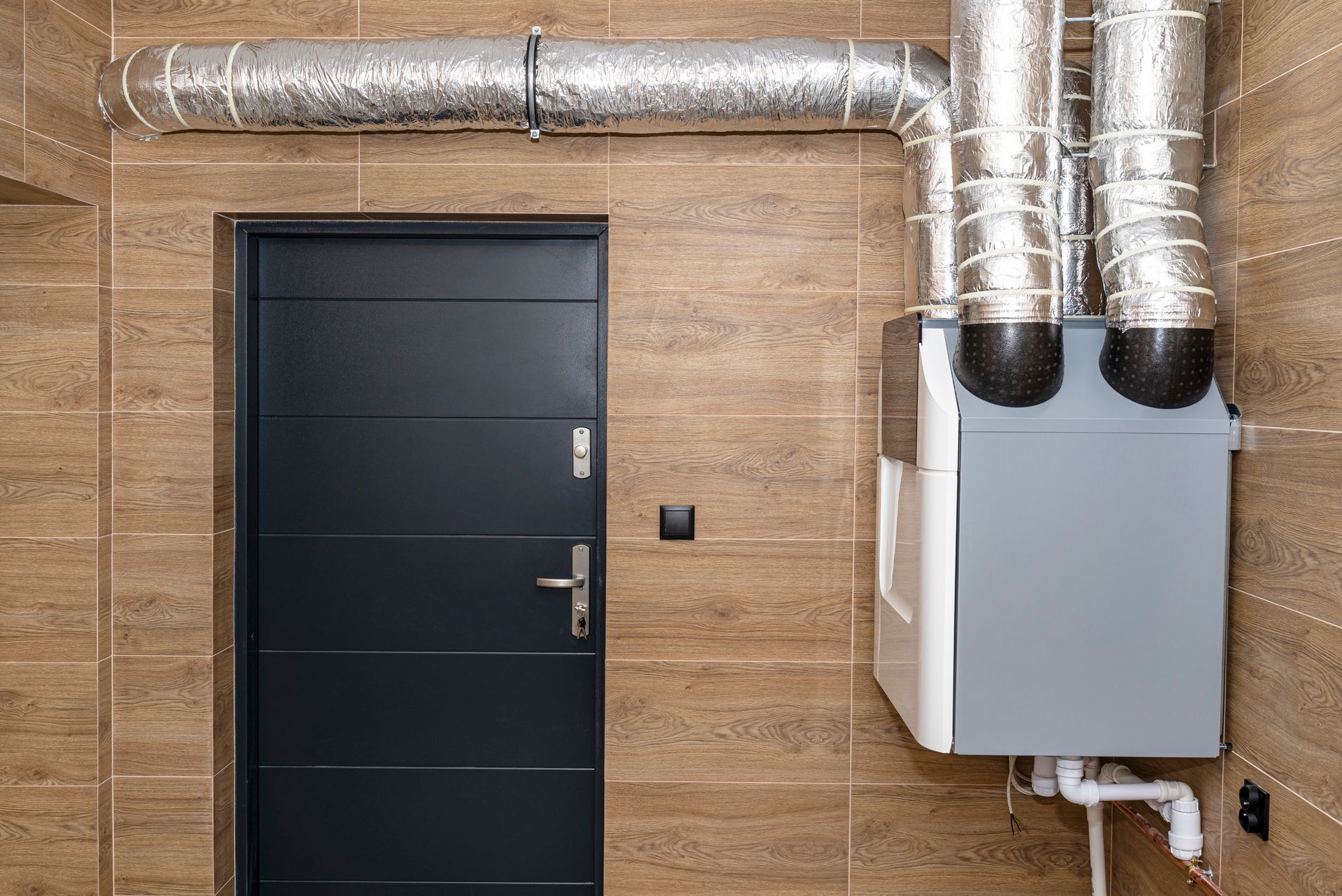 Black door on tan brick wall beside silver HVAC unit and exposed ductwork.