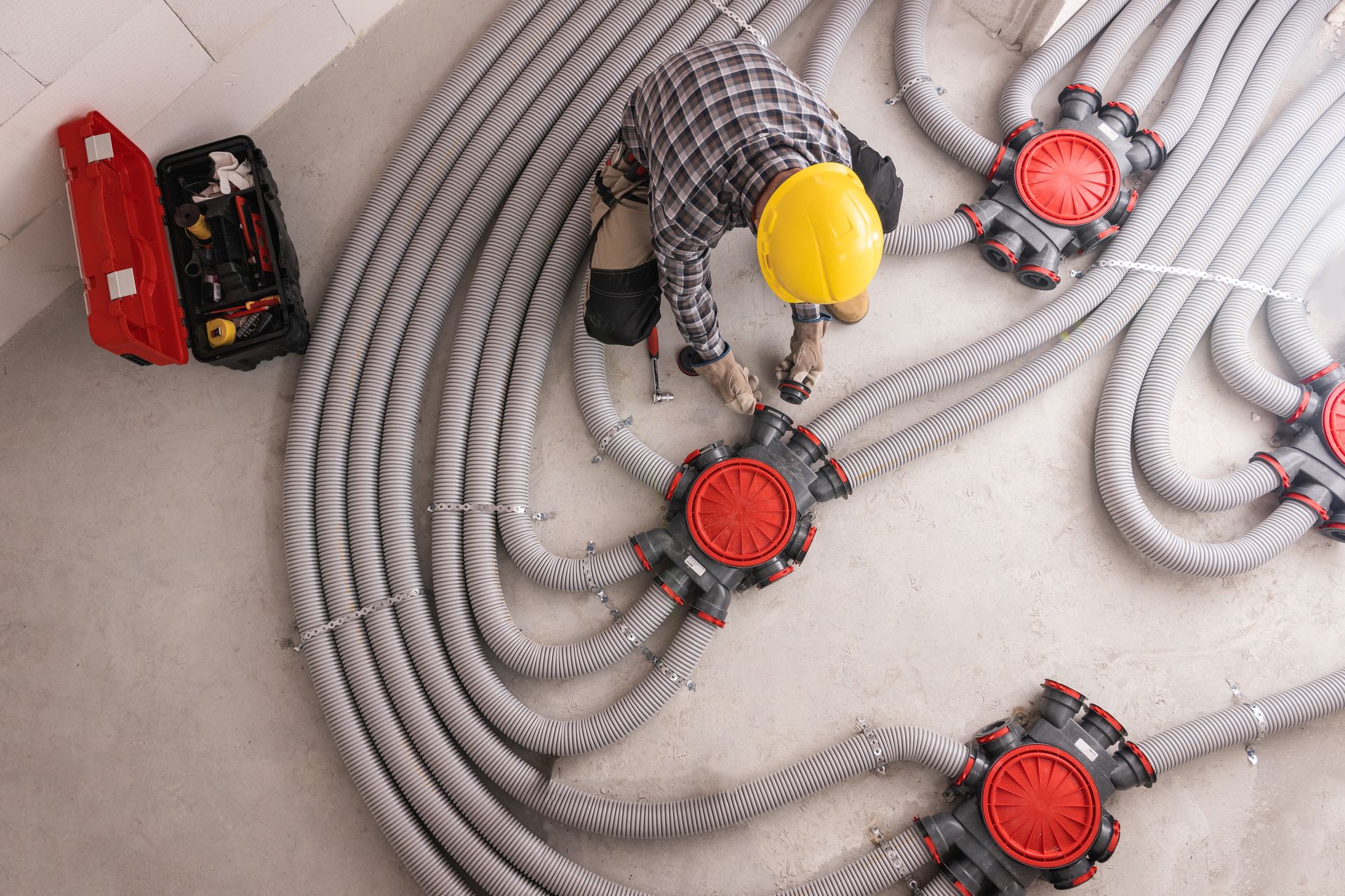 Worker in yellow hard hat inspecting bundled gray cables with red junction boxes on the floor