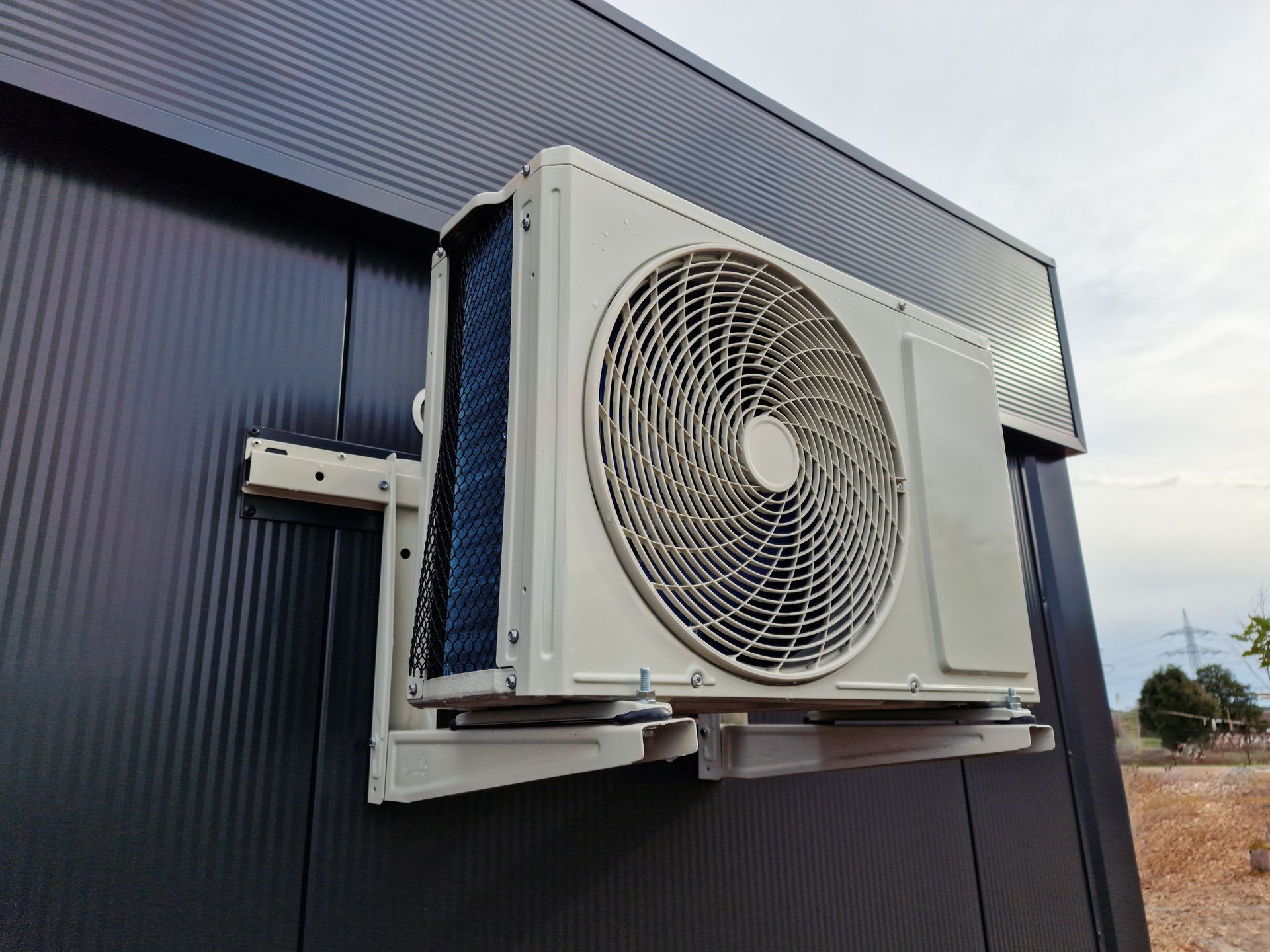 Outdoor wall-mounted air conditioner unit with a large fan on a dark metal building.
