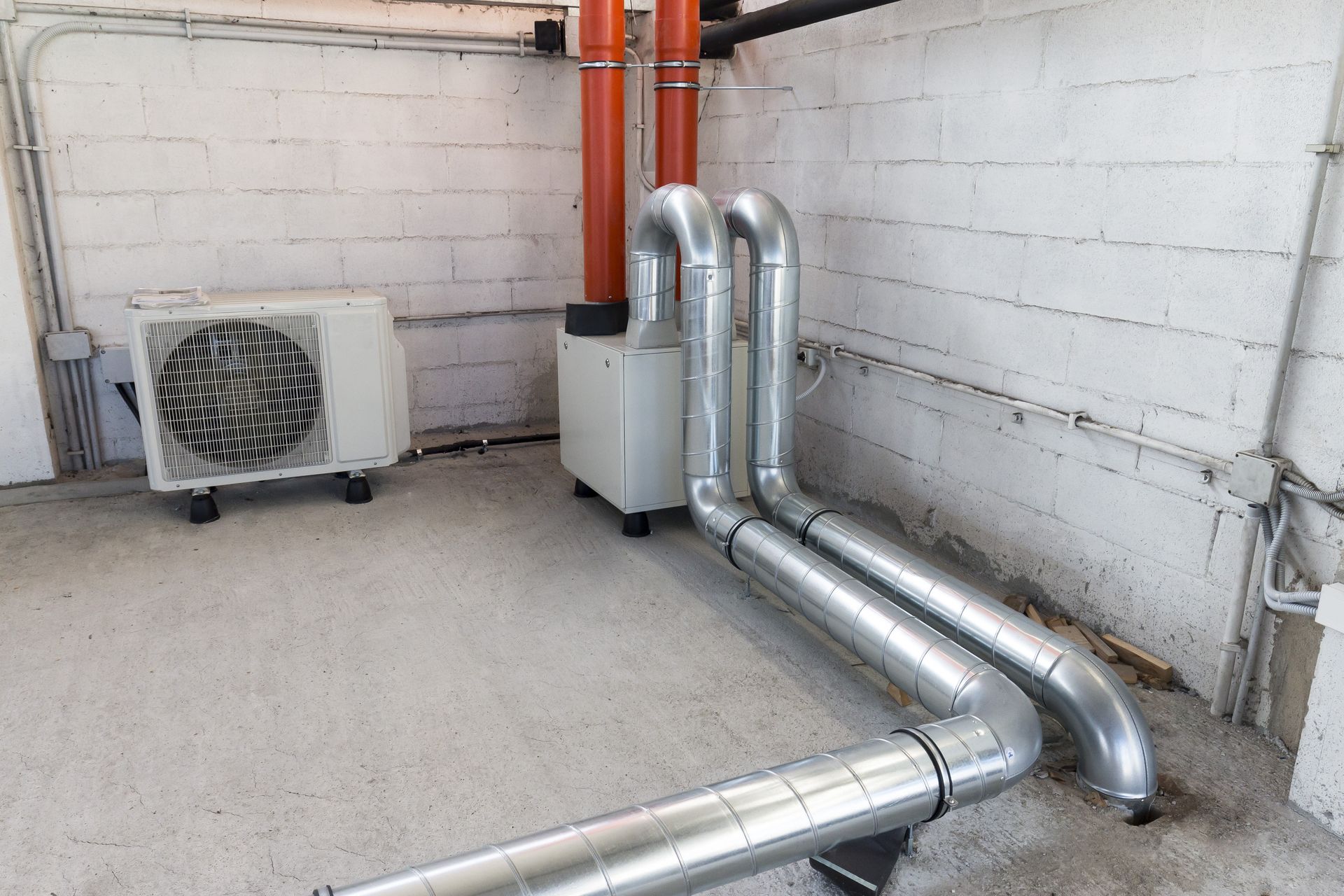 Industrial HVAC pipes and outdoor unit beside a white brick wall in a concrete utility area