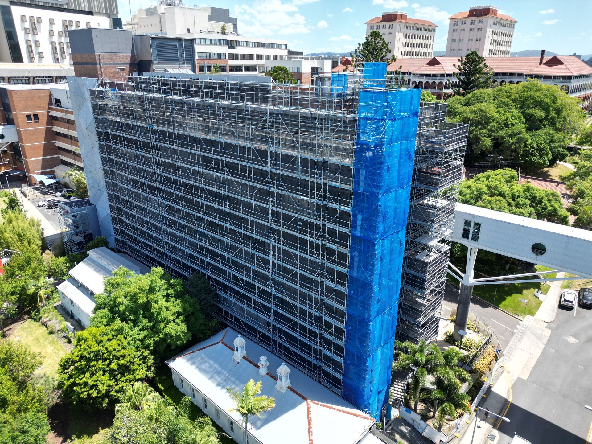 Construction site with crane reaching toward cloudy sky; building facade covered with protective netting.