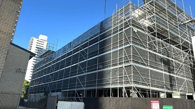 Building under construction, encased in scaffolding and black netting.