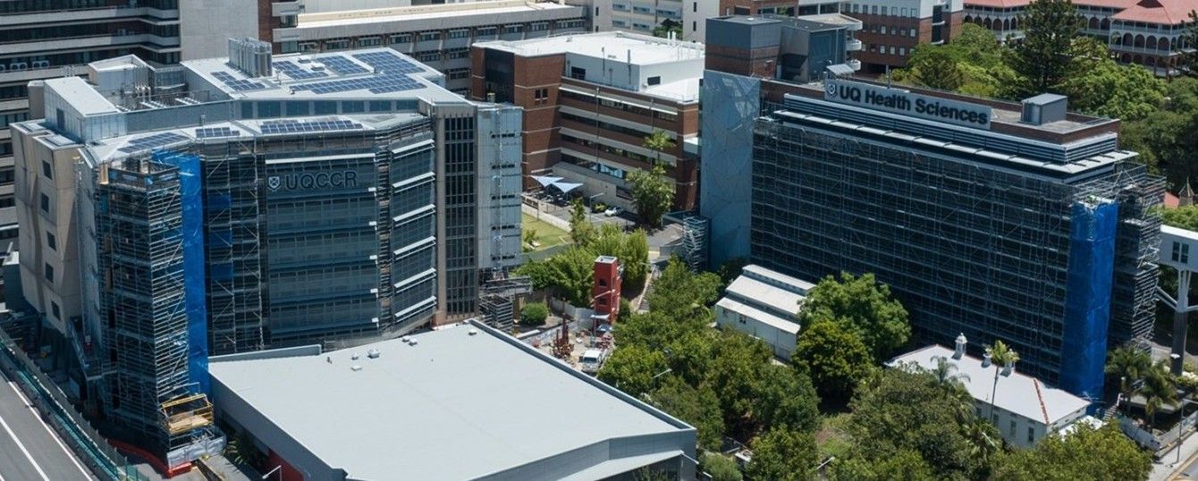 Modern high-rise apartment building with balconies and greenery, street view with cars and shops in daylight.