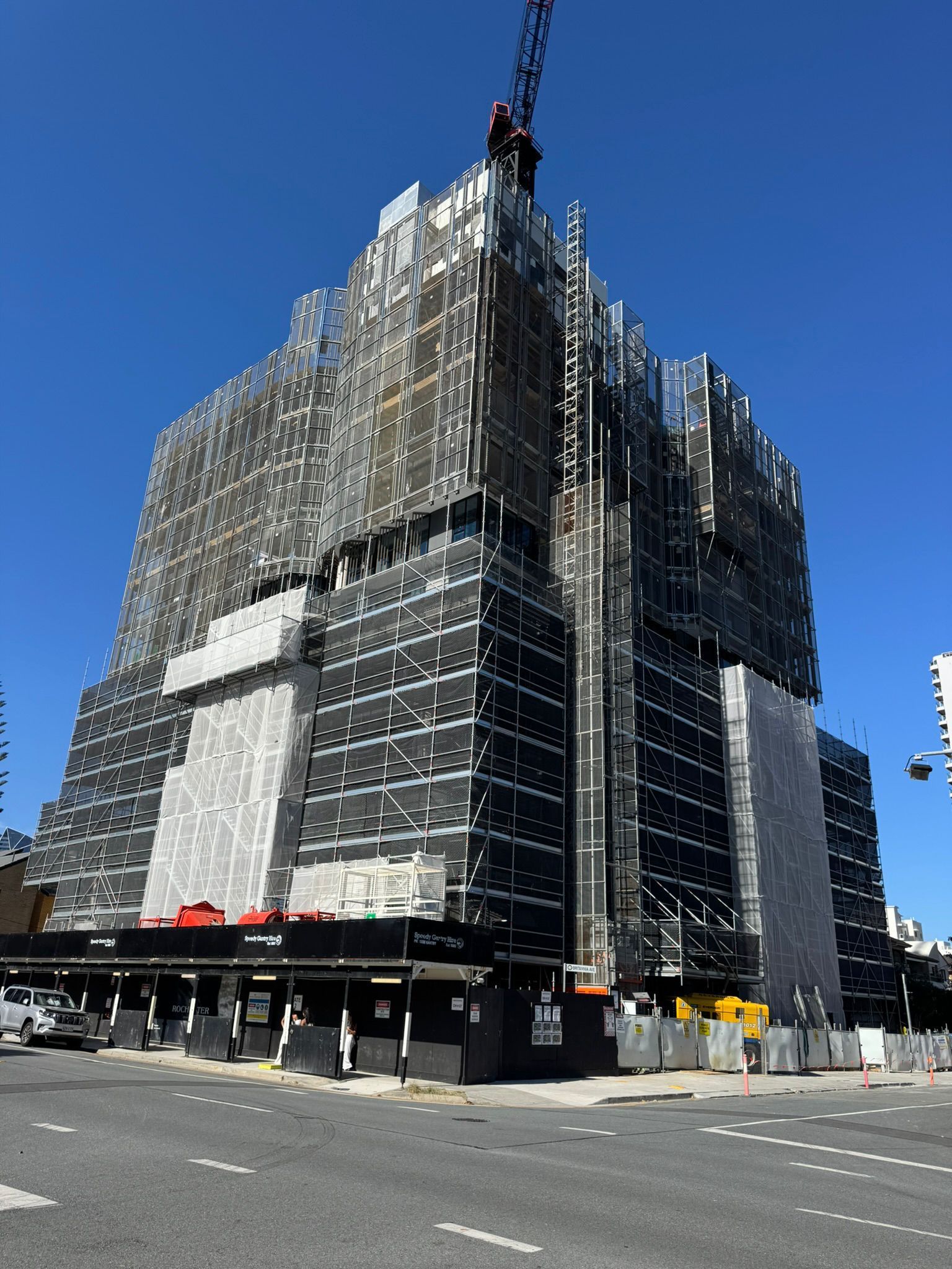 Construction of a tall high-rise building, vertical, partially completed, with a crane on top. Green and gray facade.