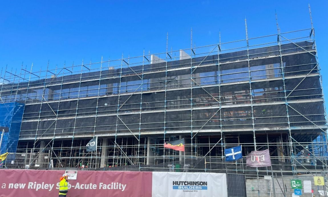 Construction site with scaffolding, safety netting, and a Hutchinson Builders banner.