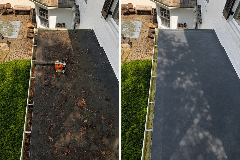 Person pressure-washing a house roof beside a brick chimney under a blue sky