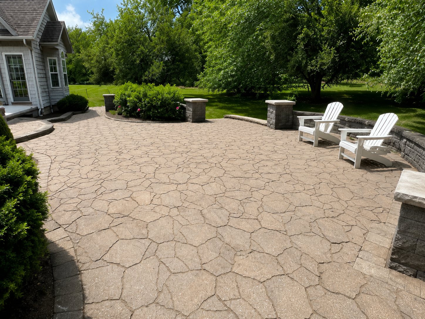 Stone patio with two white chairs, low walls, and a grassy backyard in sunlight