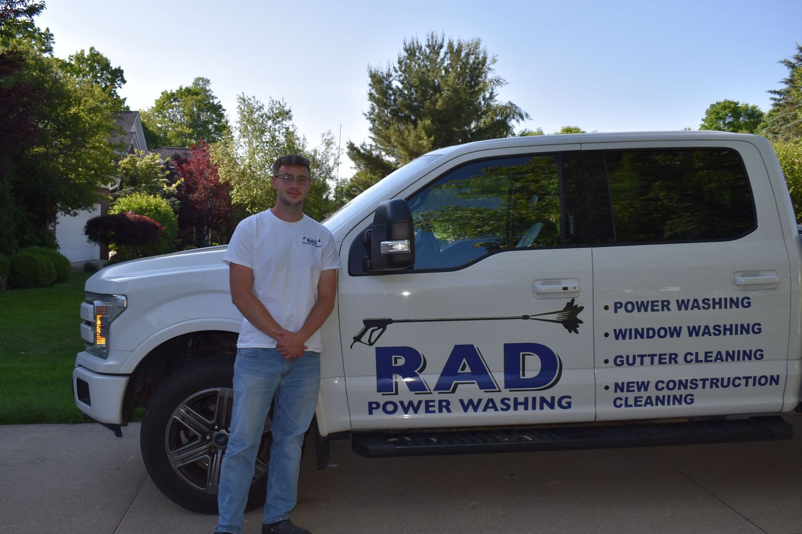 Man standing beside a white RAD Power Washing truck in a sunny residential driveway
