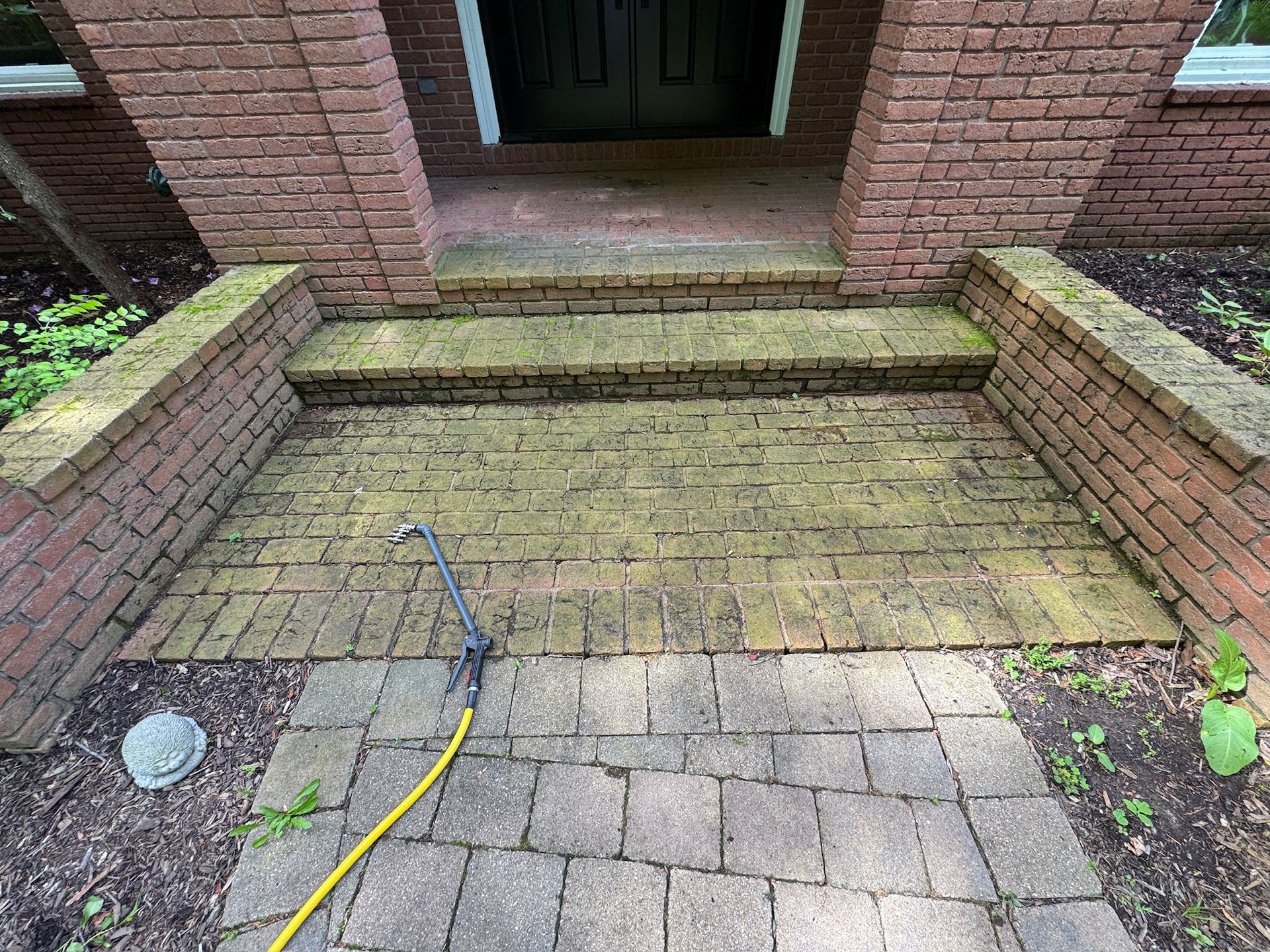 Brick front steps with a yellow hose and blue tool on a paved walkway leading to a doorway