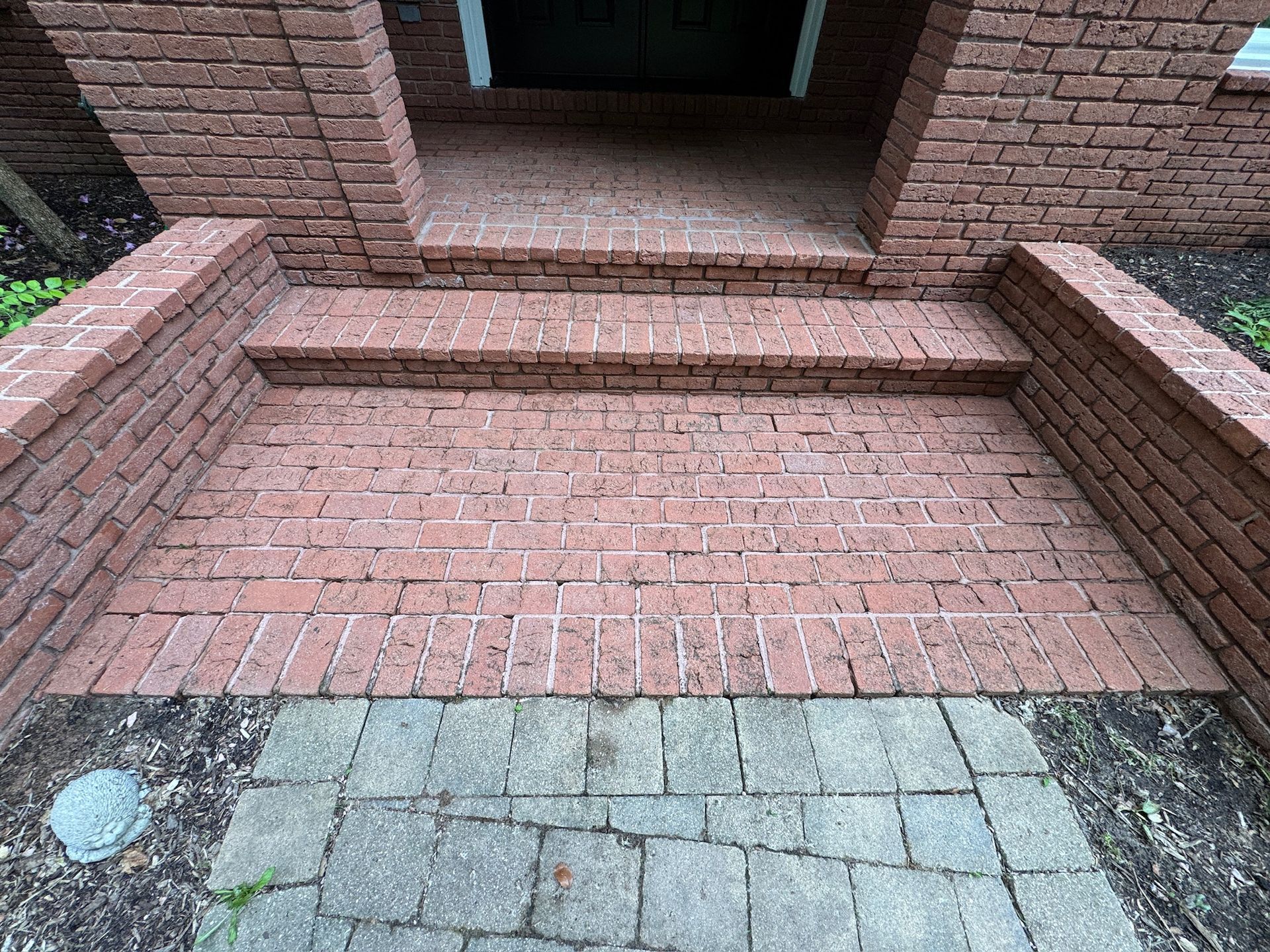 Brick steps leading to a recessed brick doorway with a gray stone walkway in front.