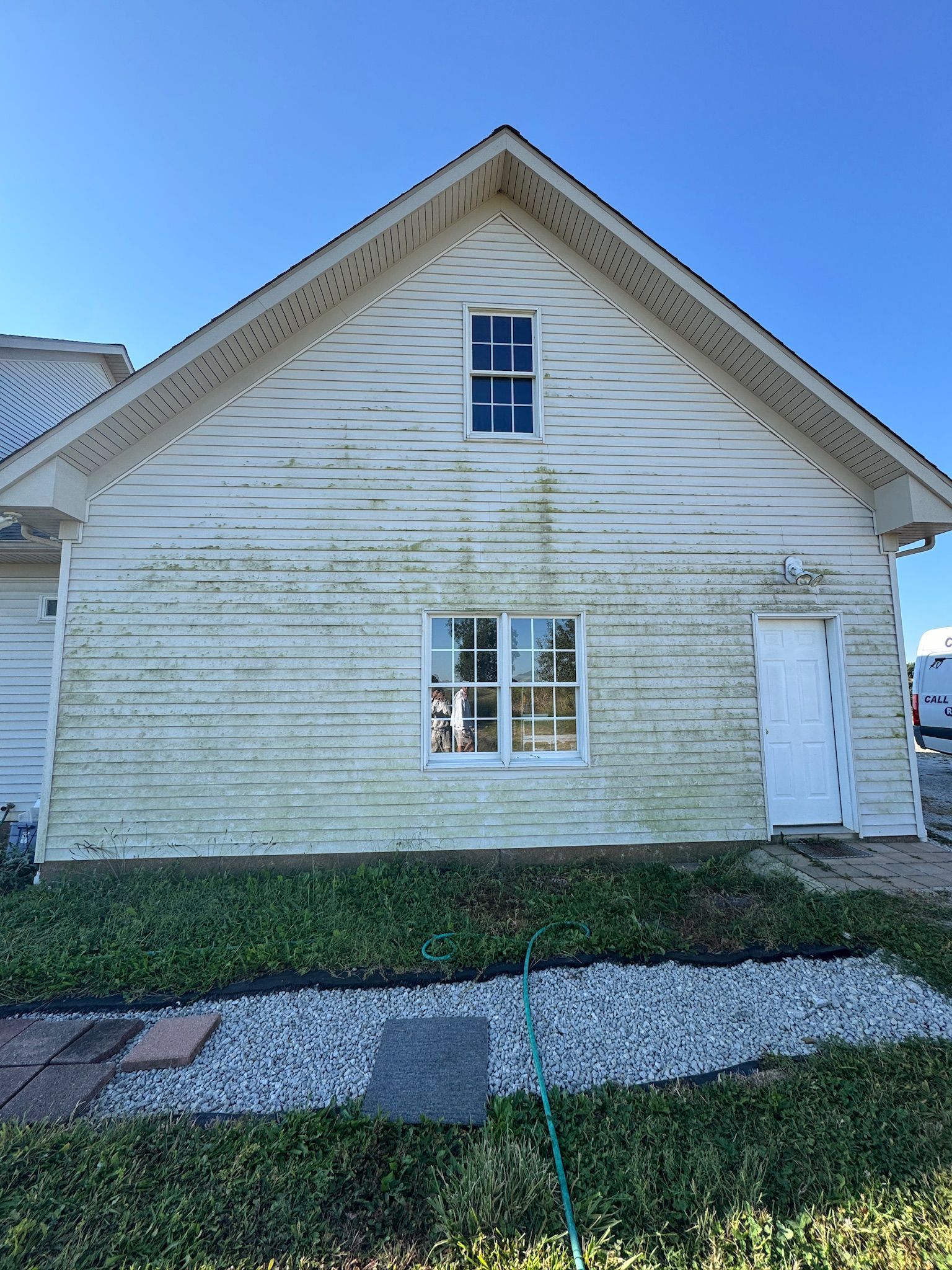Weathered white house exterior with peeling paint, front windows, and a side door under a clear blue sky.