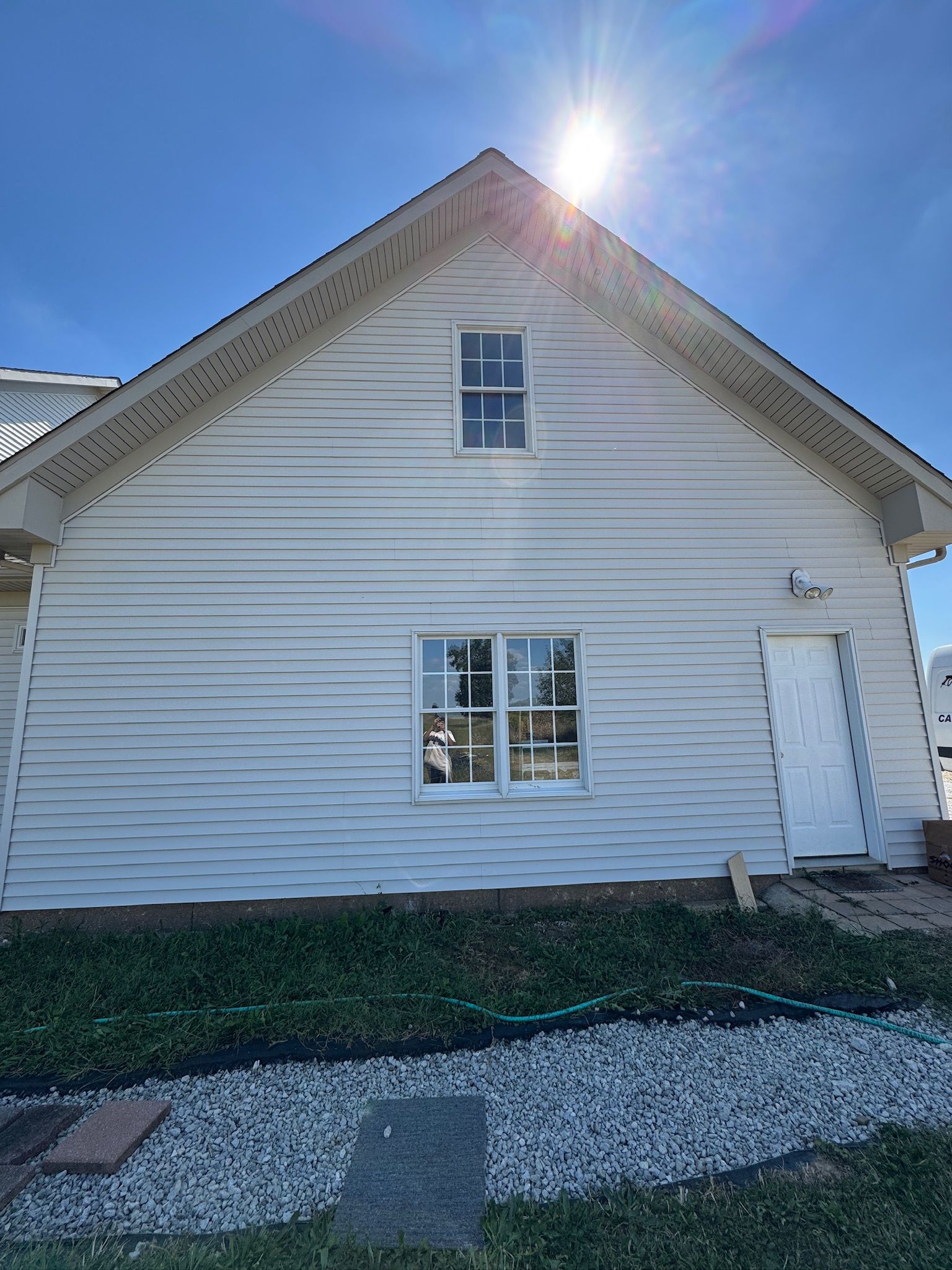 White house exterior with gabled roof, small windows, white door, and sun flaring above the roofline.