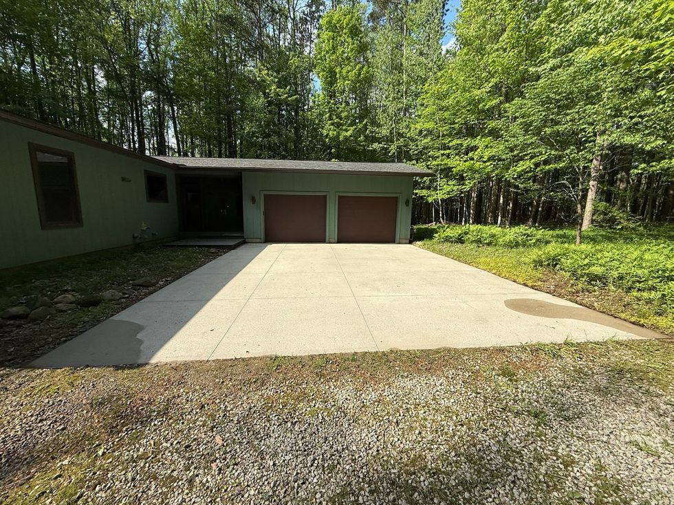 Concrete driveway leading to a garage beside a wooded house