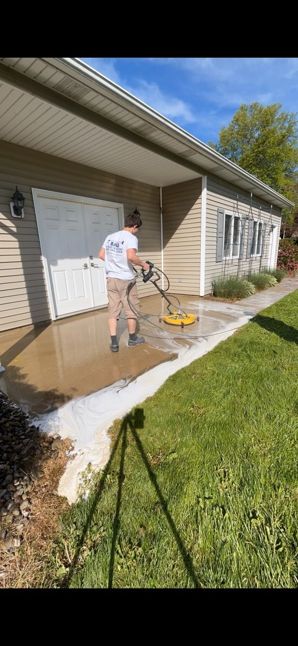 Person pressure-washing a concrete walkway beside a white house on a sunny day