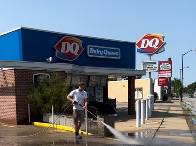 Person hosing down sidewalk outside Dairy Queen under blue awning