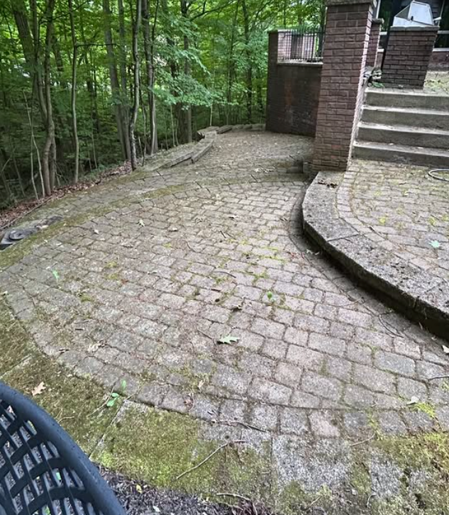 Cobblestone patio beside brick steps and a wooded area