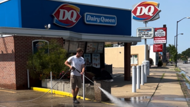 Person washing the sidewalk outside a Dairy Queen with a hose on a sunny day