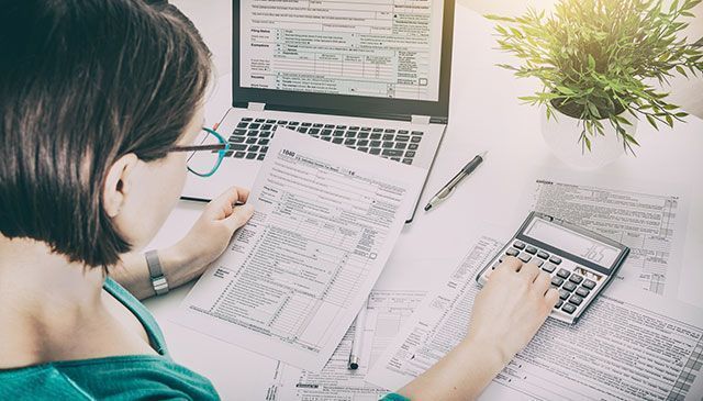 Una mujer está sentada en un escritorio usando una computadora portátil y una calculadora.