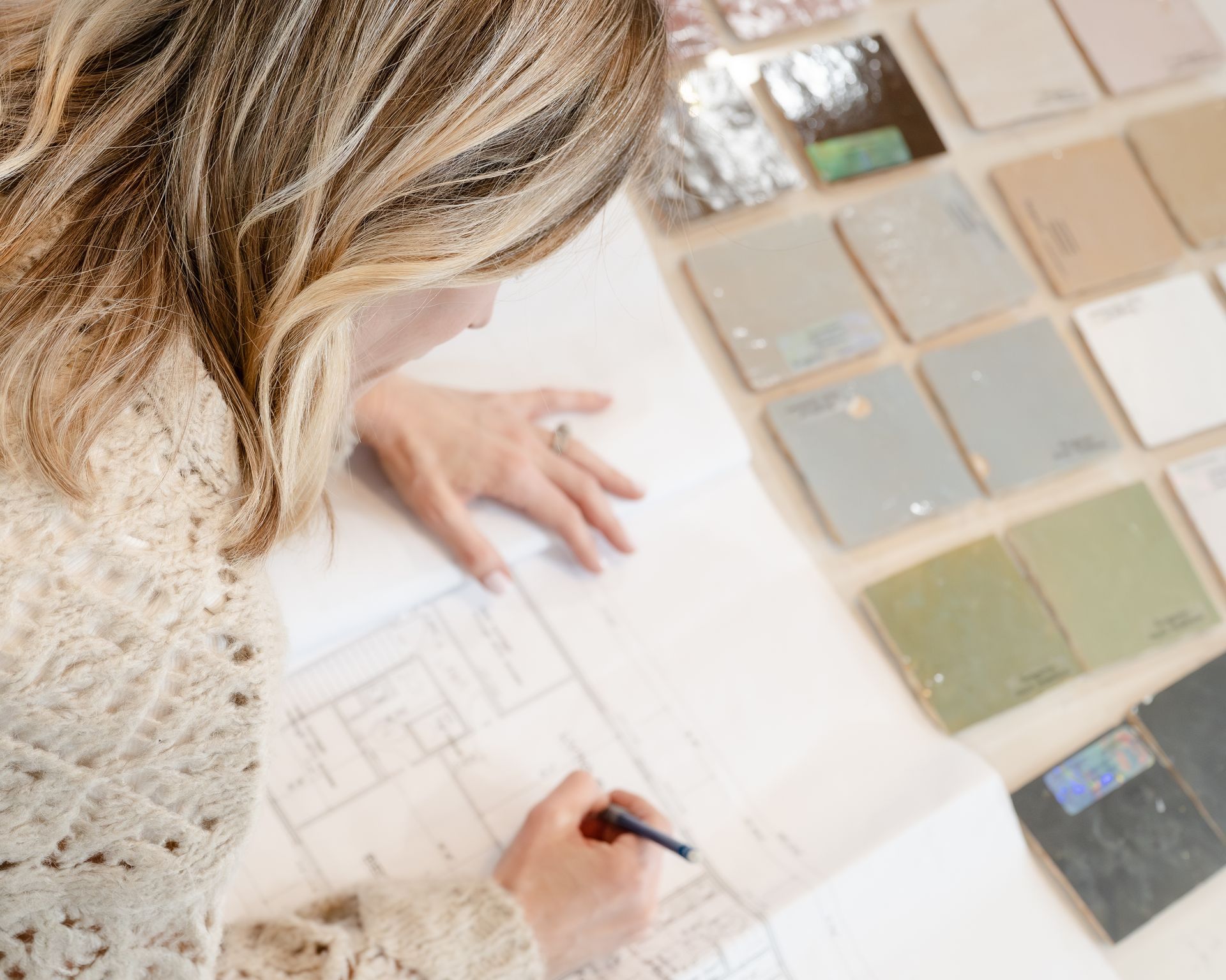 Woman drawing on floor plan with tile samples in the background.