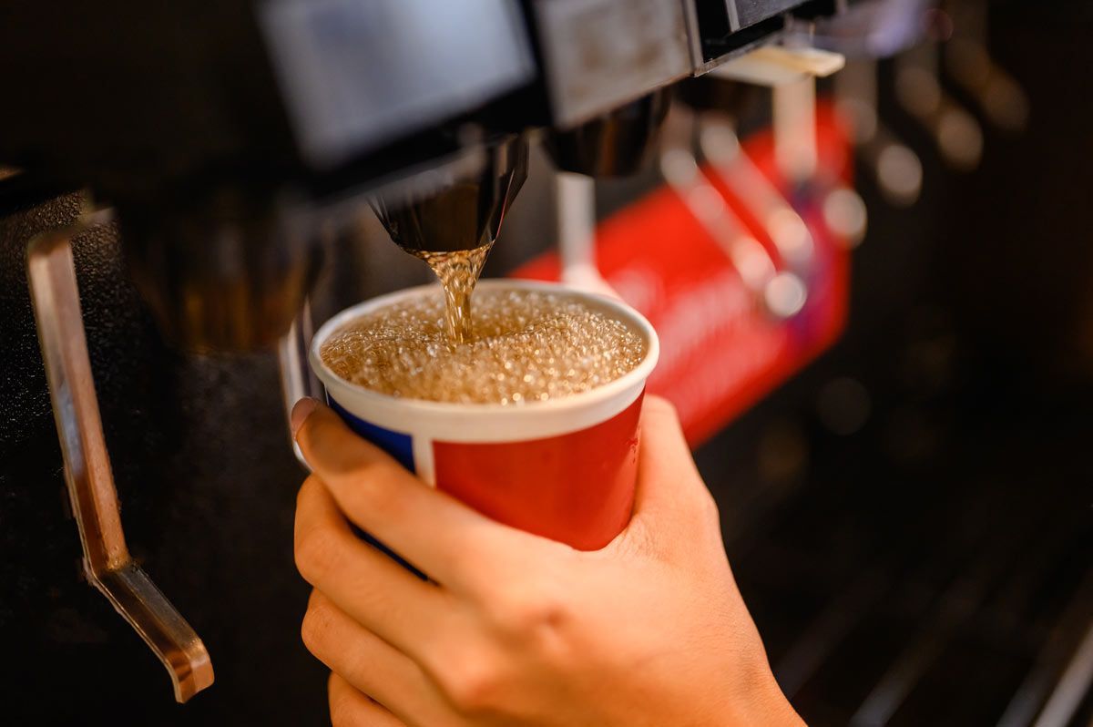closeup of a hand holding a red, white and blue cup filling it with a carbonated beverage from a machine
