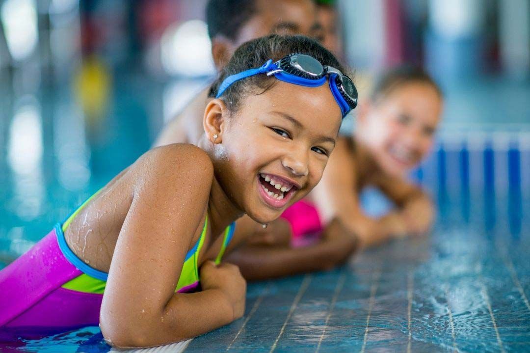 children smiling on the side of a pool 