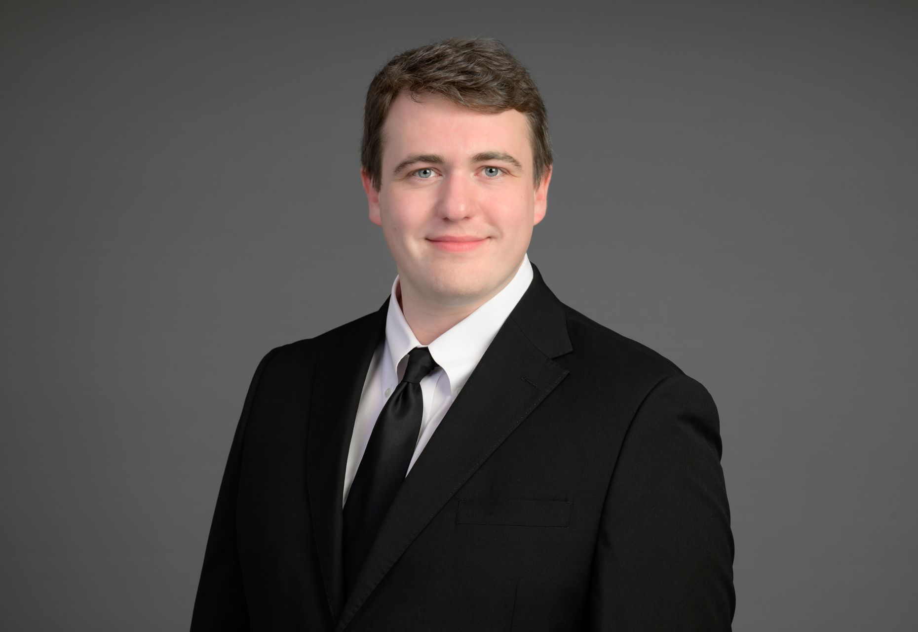 Man in a black suit and tie posing against a gray background