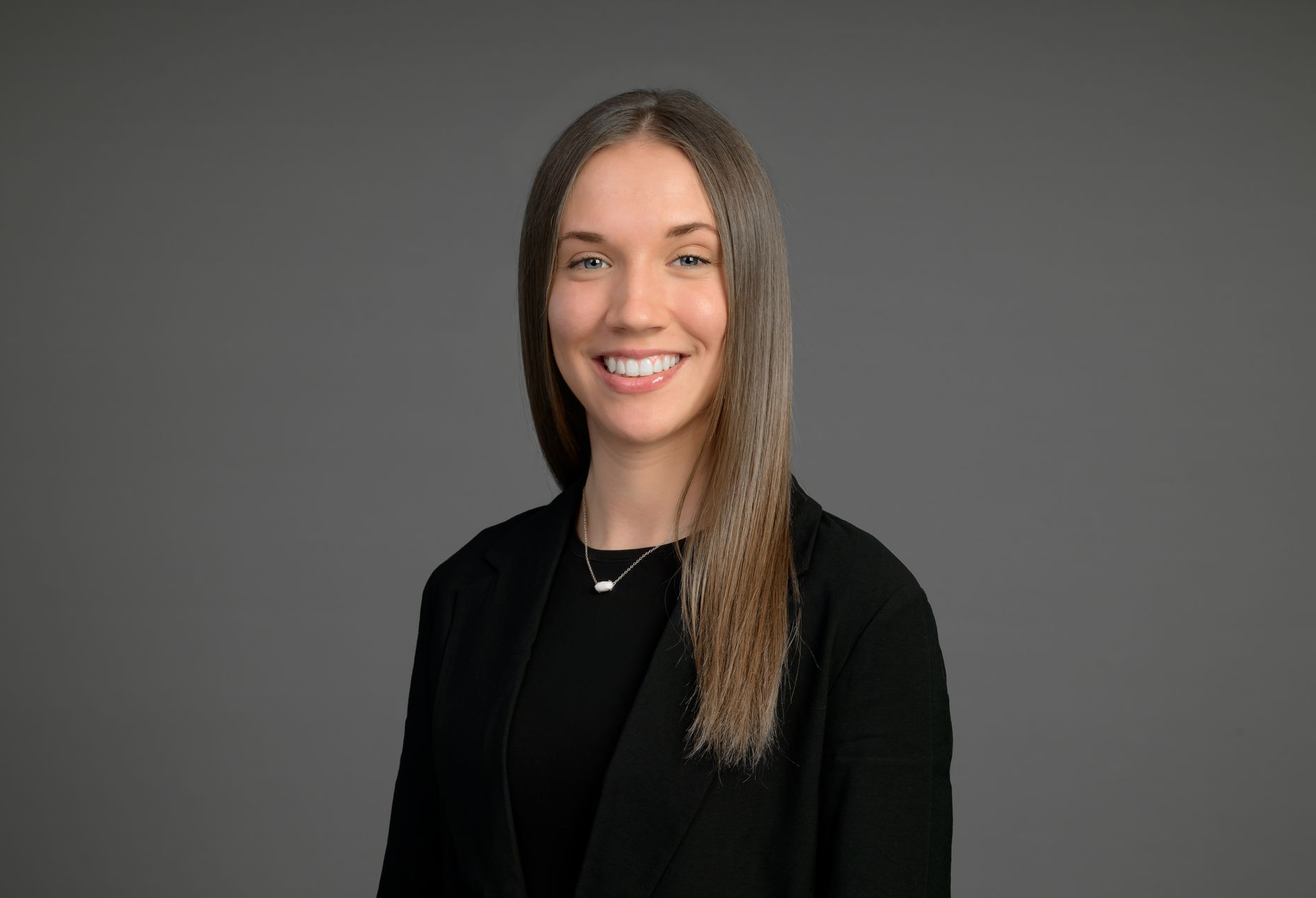 Smiling person in a black blazer against a gray background