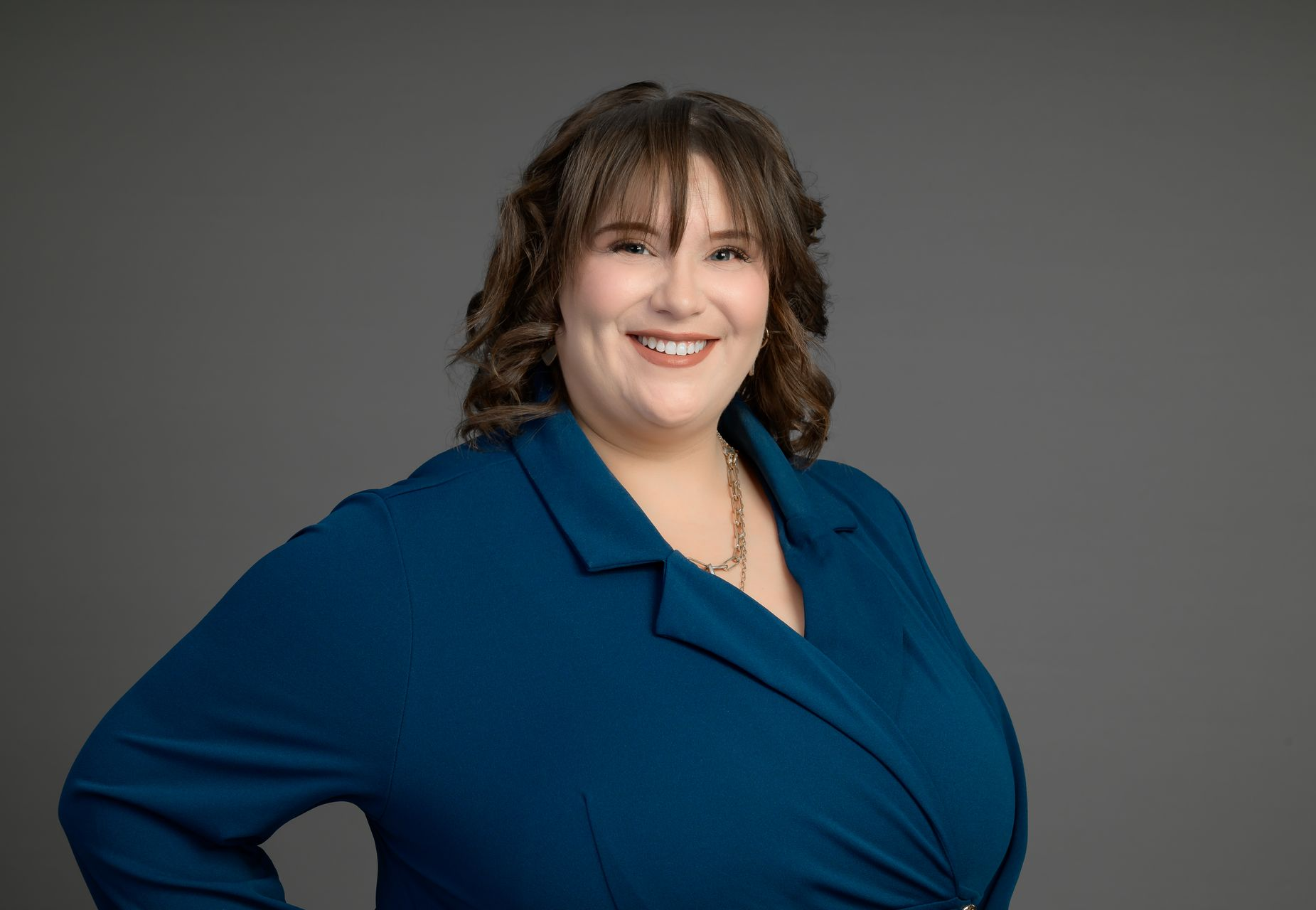 Smiling woman in a blue top posing against a gray studio background