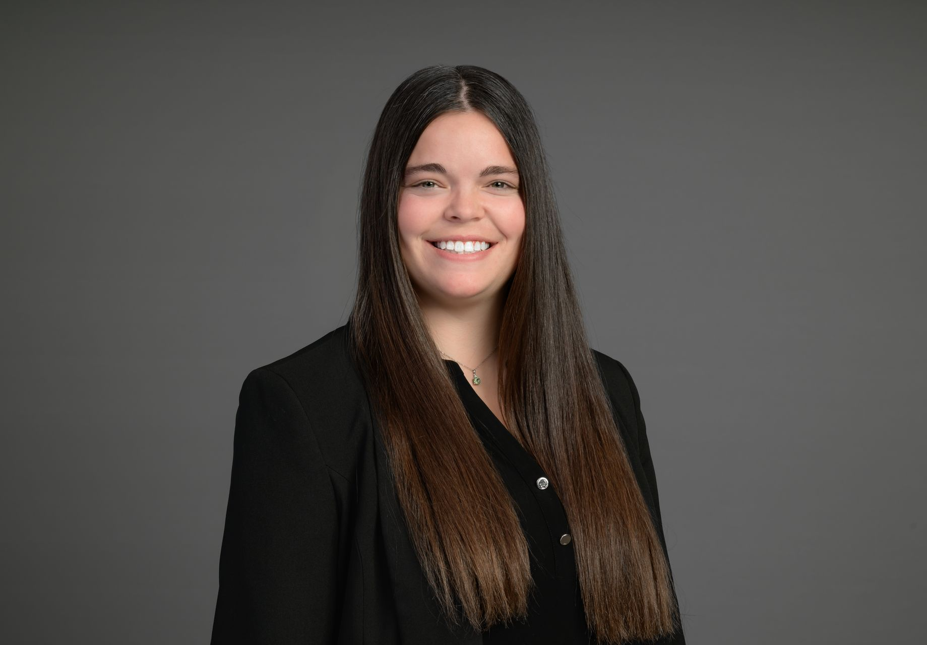 Smiling person in a black blazer against a gray background.