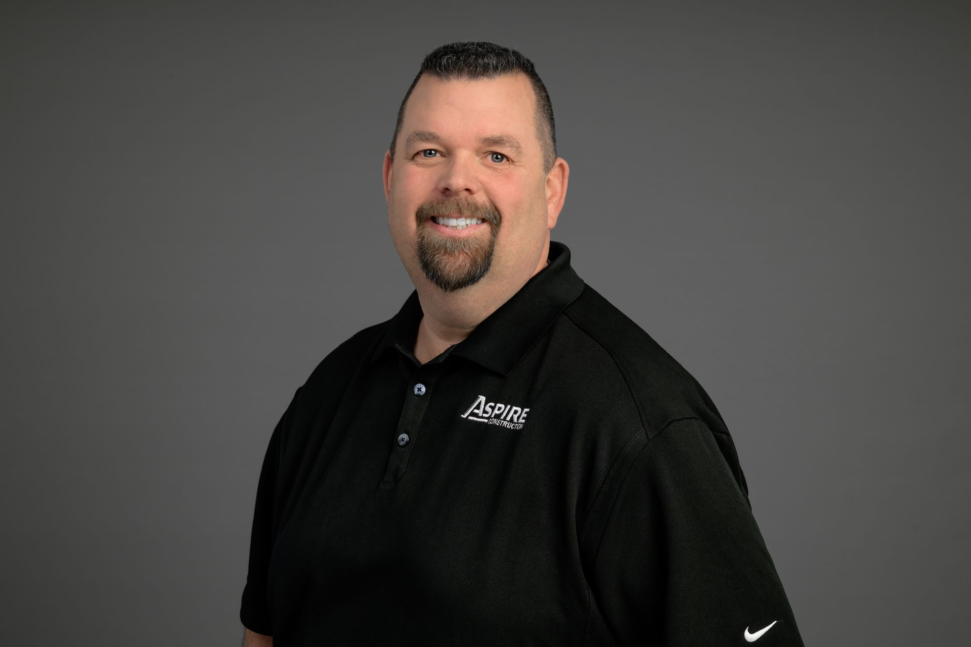 Smiling man in a black polo shirt against a gray background