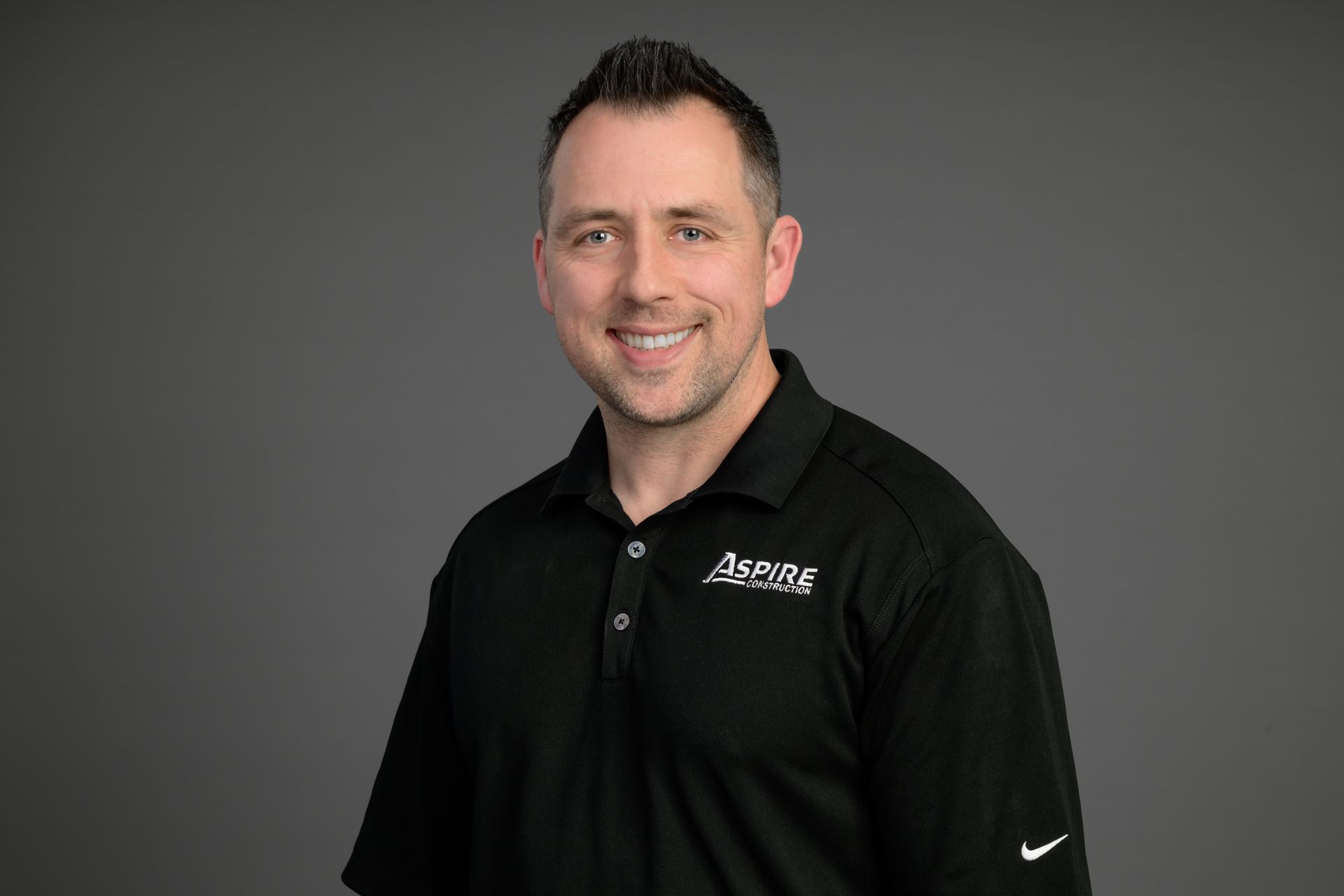 Portrait of a smiling man in a black polo shirt against a gray background