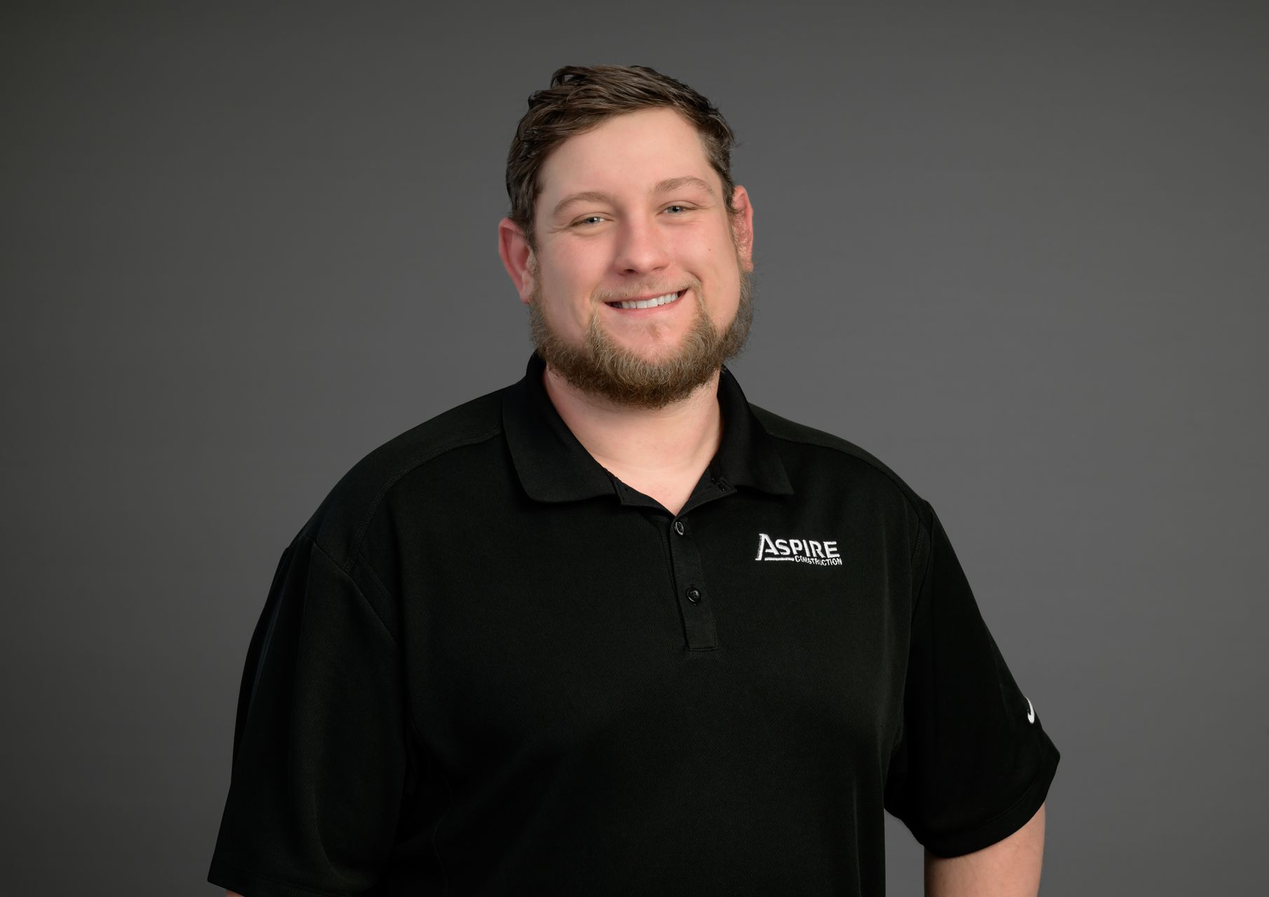 Smiling man in a black polo shirt standing against a gray background