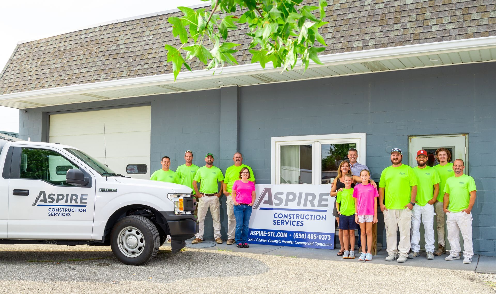 Aspire Service team posing outside a building beside a white truck and company banner
