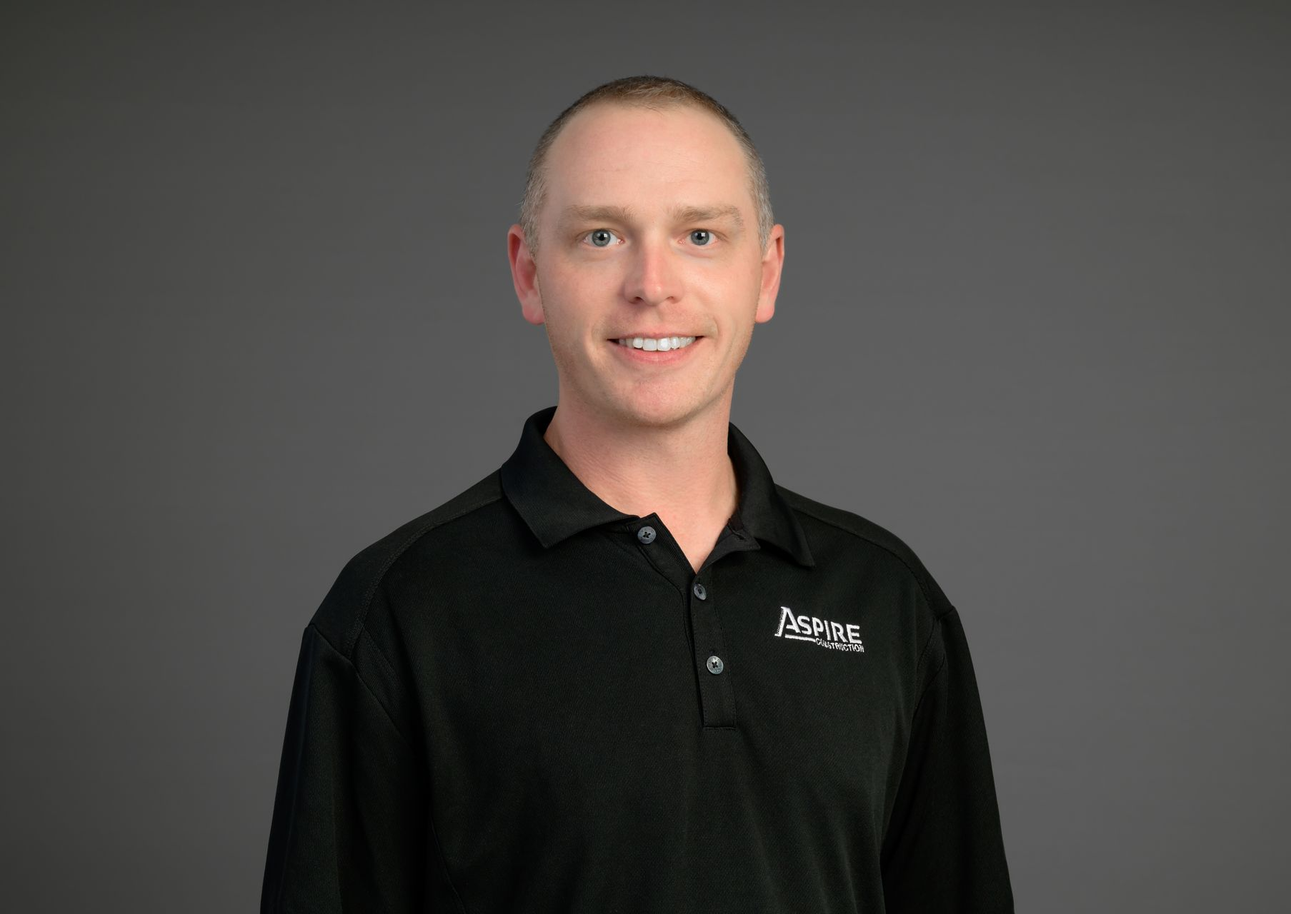 Smiling person in a black collared shirt against a gray studio background