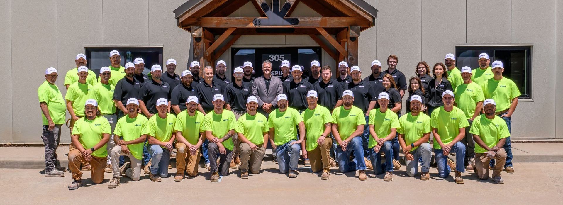 Group of volunteers in neon green and dark shirts posing in front of a wooden pavilion