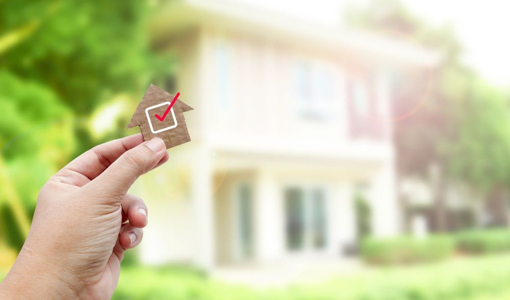 Person Holding A Small House With A Check Mark On It In Front Of A House — Pro-Vision Property Inspections In Merewether, NSW